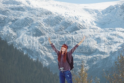 Red-hair woman raising her arms in front of snow-covered mountains background