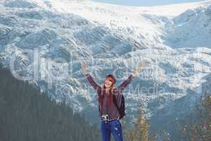 Red-hair woman raising her arms in front of snow-covered mountains background