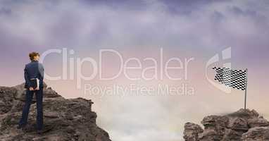 Digital composite image of businesswoman standing on rock looking at checkered flag against sky