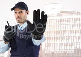 Security guard with walkie talkie and hand up against faded buildings