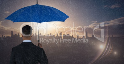 Back of business man with umbrella against skyline with sunset