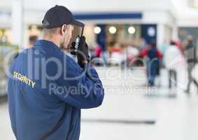 Back of security guard with walkie talkie against blurry shopping centre