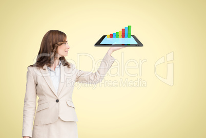 Business woman is holding a tablet computer projecting holograms against yellow background