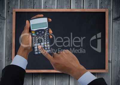 Hands with calculator against chalkboard and grey wood panel