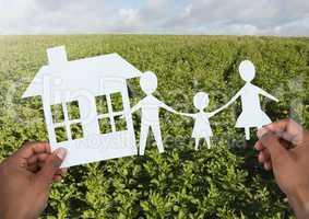 Cut outs house and family in hands over landscape