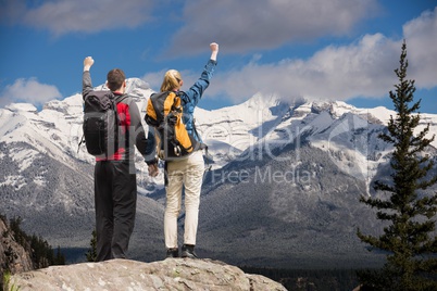 Couple raising their hands on the top of mountains in front of snow-covered mountains