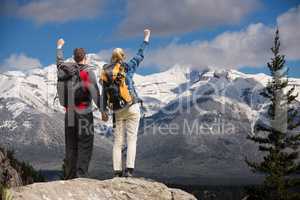 Couple raising their hands on the top of mountains in front of snow-covered mountains