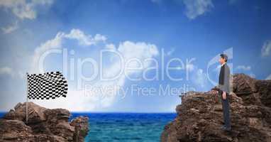 Digital composite image of businessman standing on rock looking at checkered flag standing against s