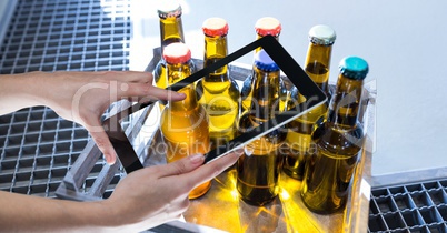 Hands photographing beer bottles through digital tablet at brewery