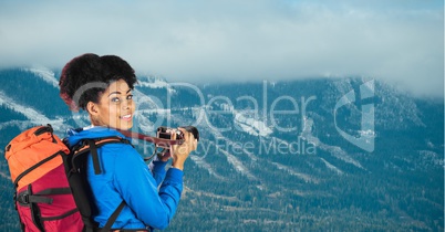 Portrait of smiling hiker with camera standing against mountains