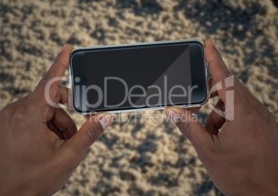 Hands with phone against blurry sand