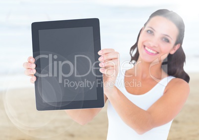 Smiling woman holding out tablet against blurry beach with flare