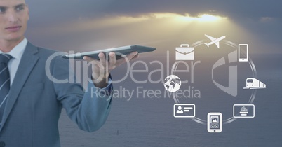 Businessman holding tablet with business icons against soft grey sky with sunshine