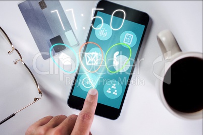 Hand touching icon on smartphone screen against credit card, glasses and cup of coffee background