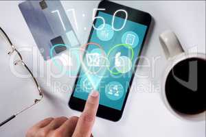 Hand touching icon on smartphone screen against credit card, glasses and cup of coffee background