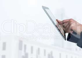 Businessman holding tablet in front of bright buildings