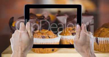 Cropped hands photographing muffins through digital tablet at bakery