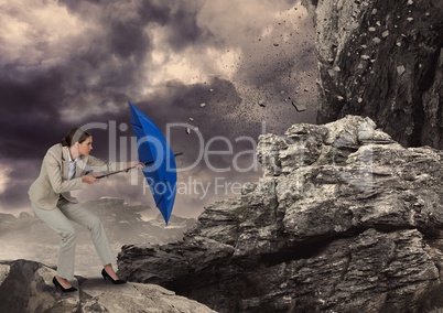 Digital image of rocks falling on businesswoman with blue umbrella standing against sky