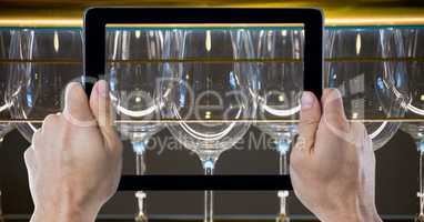 Hands photographing wine glasses through digital tablet at bar