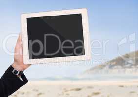 Hand with tablet against blurry beach