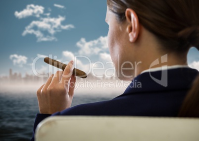 Over shoulder of seated business woman smoking cigar and looking at blurry skyline and water