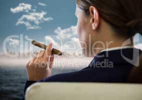 Over shoulder of seated business woman smoking cigar and looking at blurry skyline and water