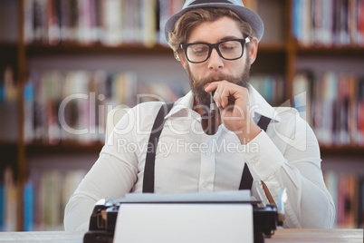 Hipster man with hat, pipe and glasses reflecting on his typewriter