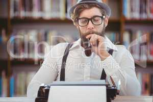 Hipster man with hat, pipe and glasses reflecting on his typewriter