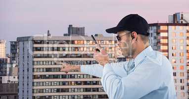 Security guard holding walkie talkie pointing against buildings