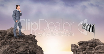 Businessman looking at checkered flag while standing on rocks against sky