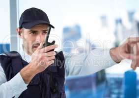 Security guard with walkie talkie pointing against blurry window showing city