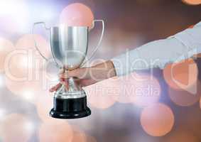 Hand holding trophy cup with sparkling light bokeh background