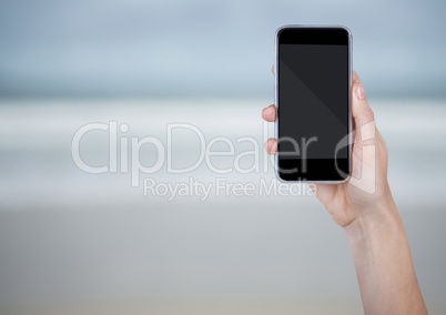 Hand with phone against blurry beach