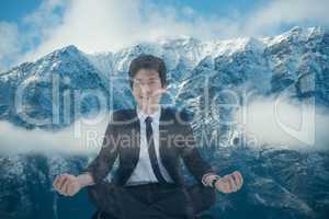 Businessman doing yoga position in front of snow-covered mountains