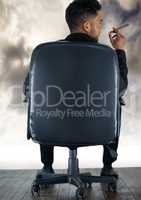 Back of seated business man smoking cigar against clouds and wood floor