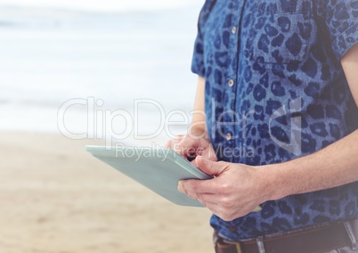 Trendy man mid section with tablet against blurry beach