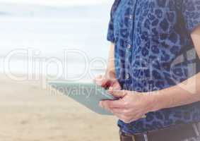 Trendy man mid section with tablet against blurry beach