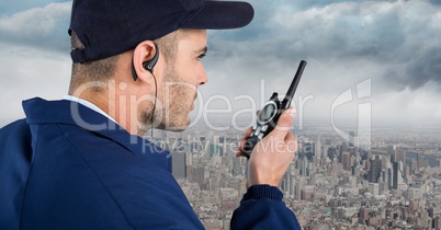 Security guard with cap and walkie talkie against skyline and clouds