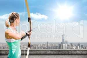 A woman archer is holding a bow and is ready to throw one narrow on cityscape background
