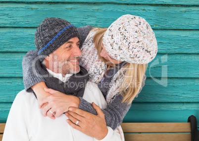 couple smiling and looking each other in a bench with light blue wood background
