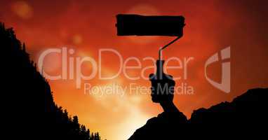 Silhouette image of hand holding paint roller against red sky
