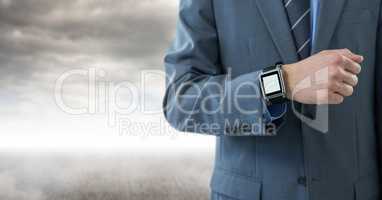 Businessman with watch against cloudy background