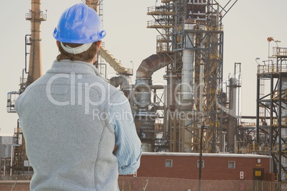 Engineer wearing blue safety helmet is looking at oil refinery from the back against oil refinery ba