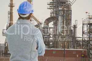 Engineer wearing blue safety helmet is looking at oil refinery from the back against oil refinery ba