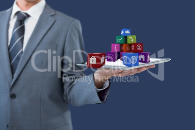 Business man holding a tablet computer projecting icons holograms against blue background