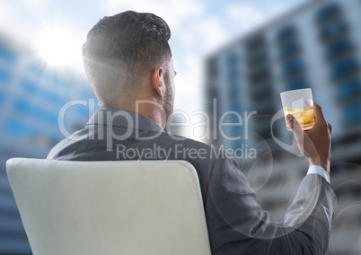 Back of seated business man drinking and looking at blurry buildings with flare