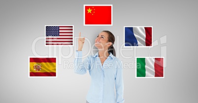Smiling businesswoman pointing upwards standing by flags against gray background