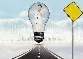 Digital composite image of smiling businesswoman in light bulb over road by signboard