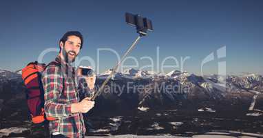 Hipster carrying backpack with camera and taking selfie while standing against mountains