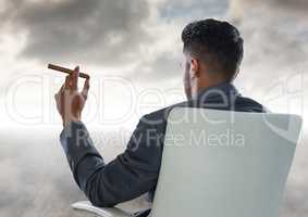 Back of seated business man smoking cigar and looking at clouds